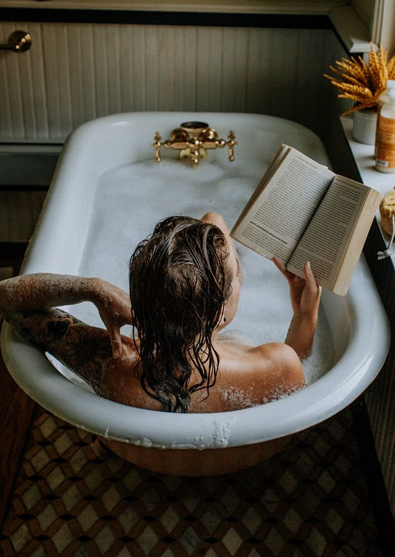 Woman relaxing in a vintage bathtub reading a book, editorial lifestyle portrait