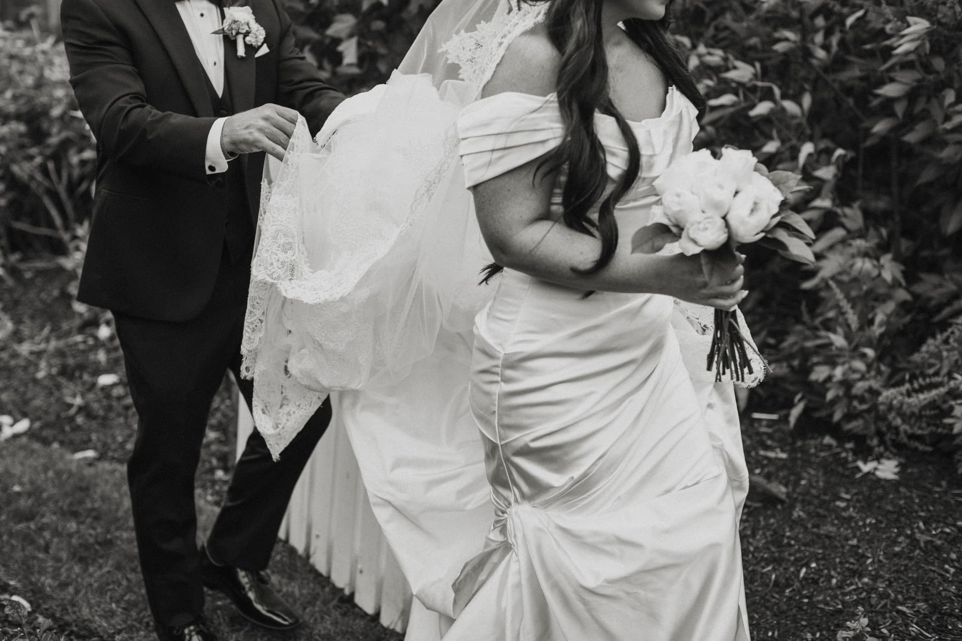 Black and white photo of a groom lifting the bride's lace veil as she holds her bouquet