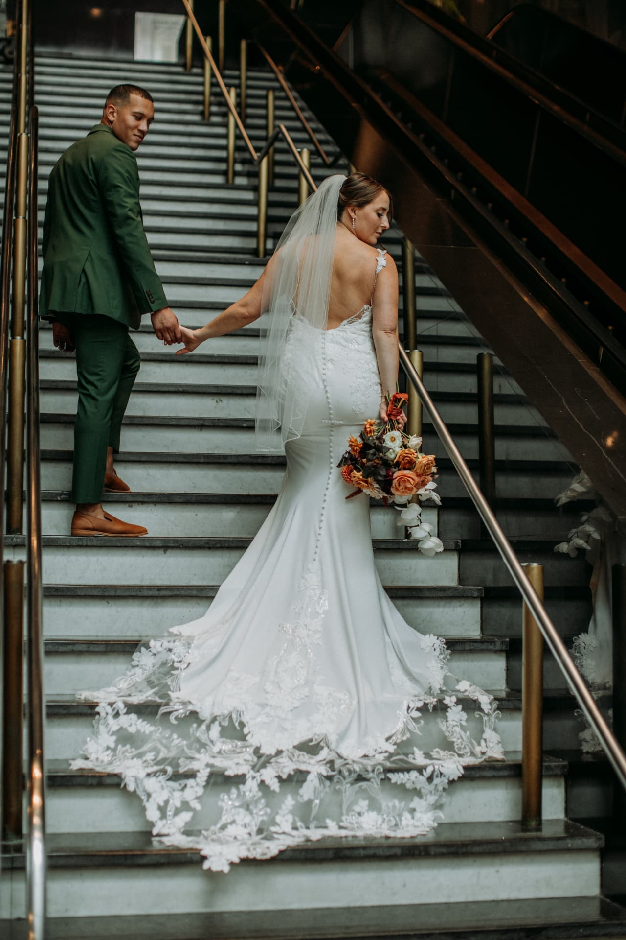 Bride with a long lace train being led up a staircase by her groom
