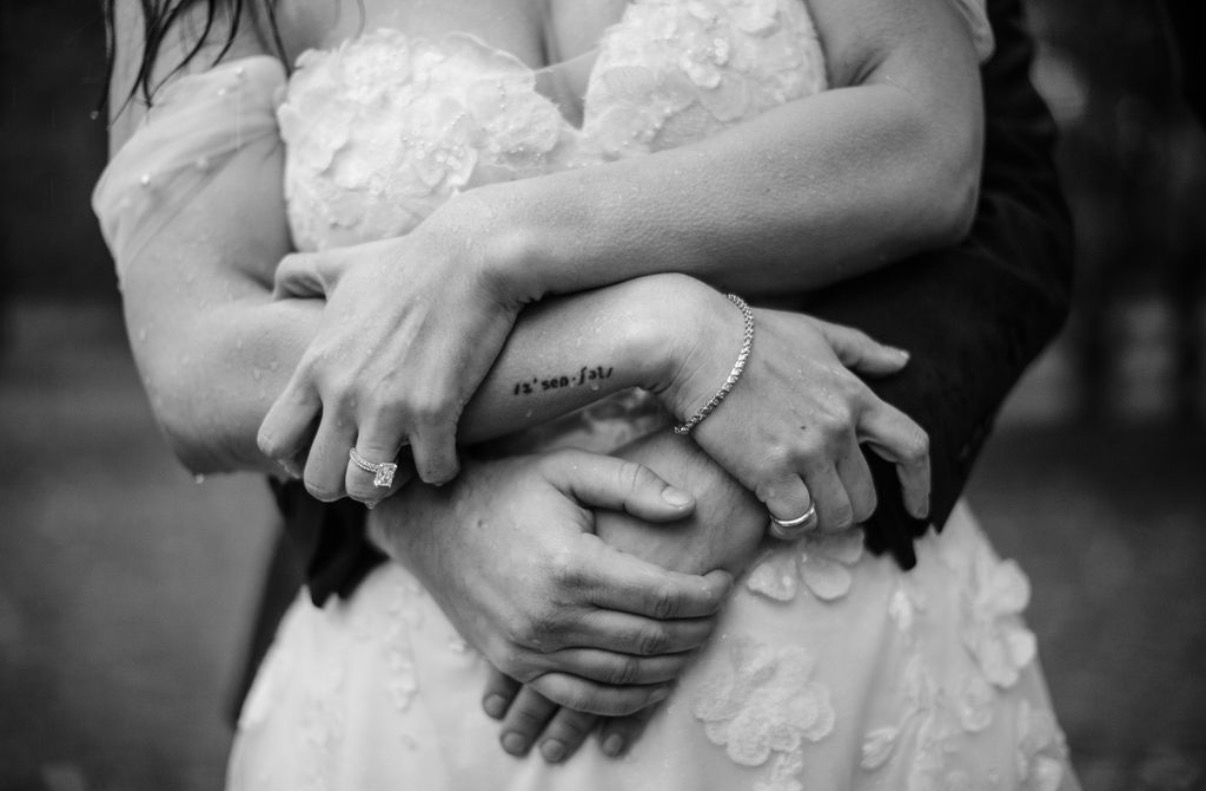Black and white close-up of a bride and groom's hands wrapped together in the rain