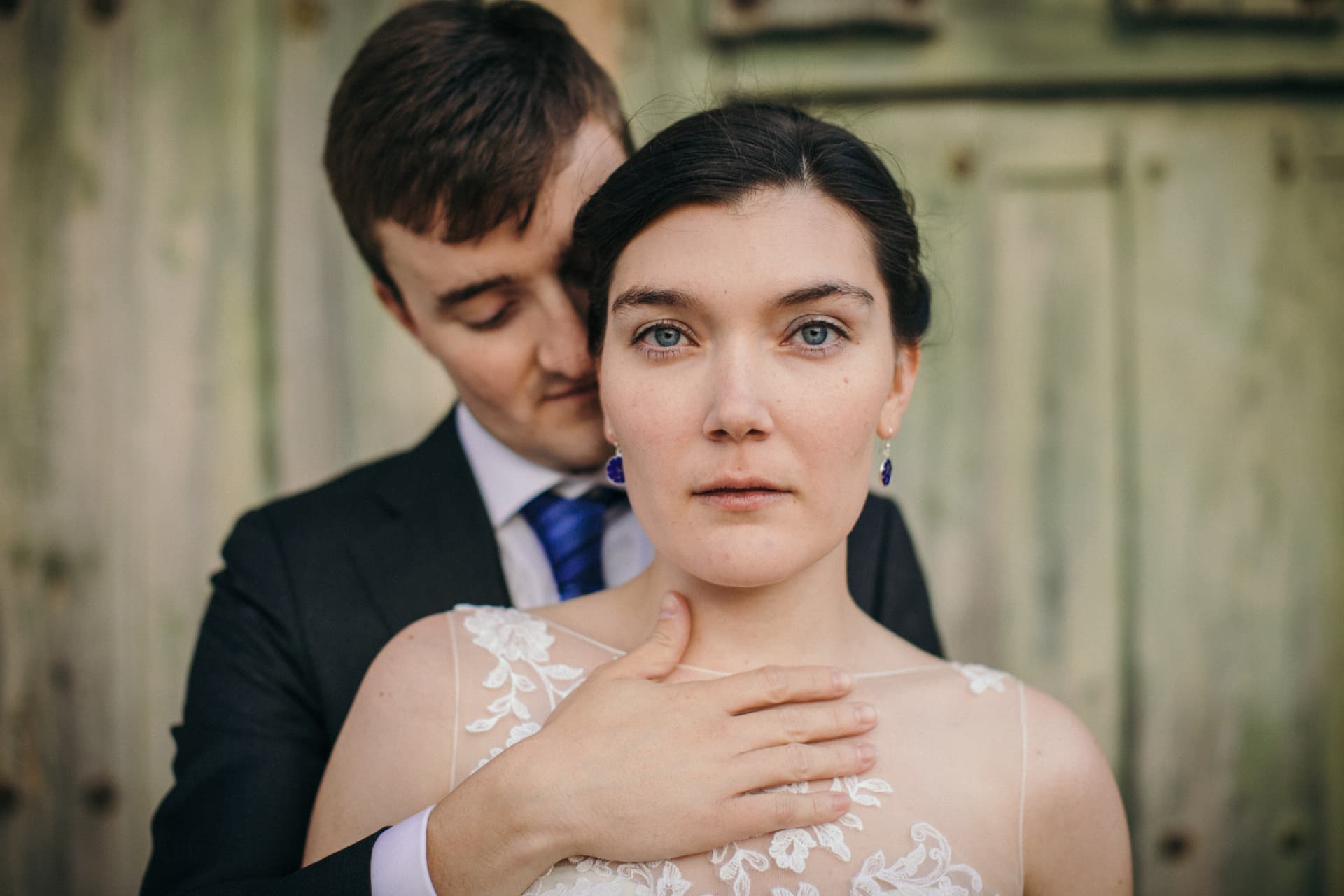 Portrait of a groom embracing his bride in front of a weathered green door