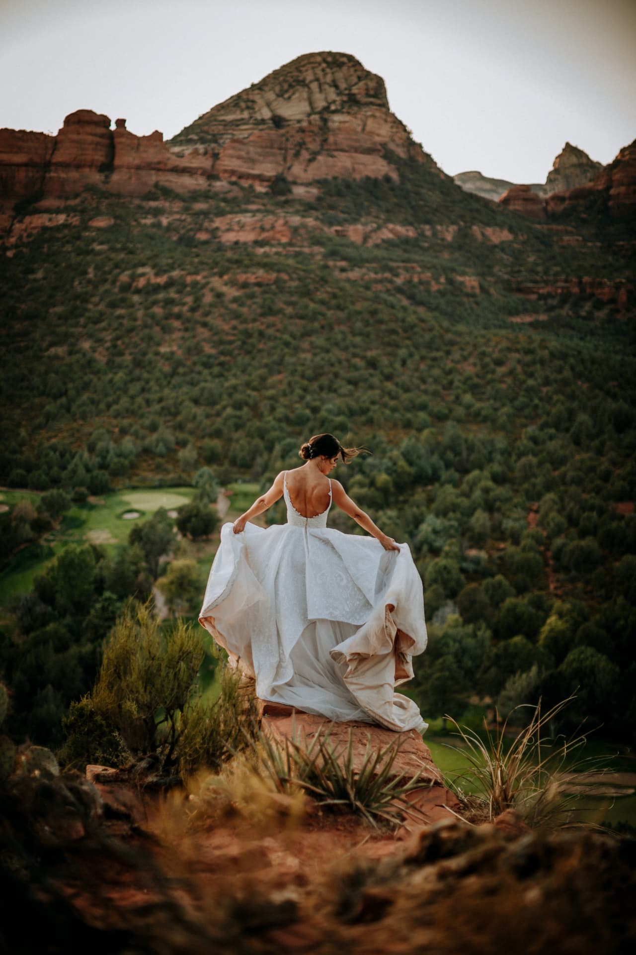 Bride seen from behind holding her gown against the Sedona red rocks