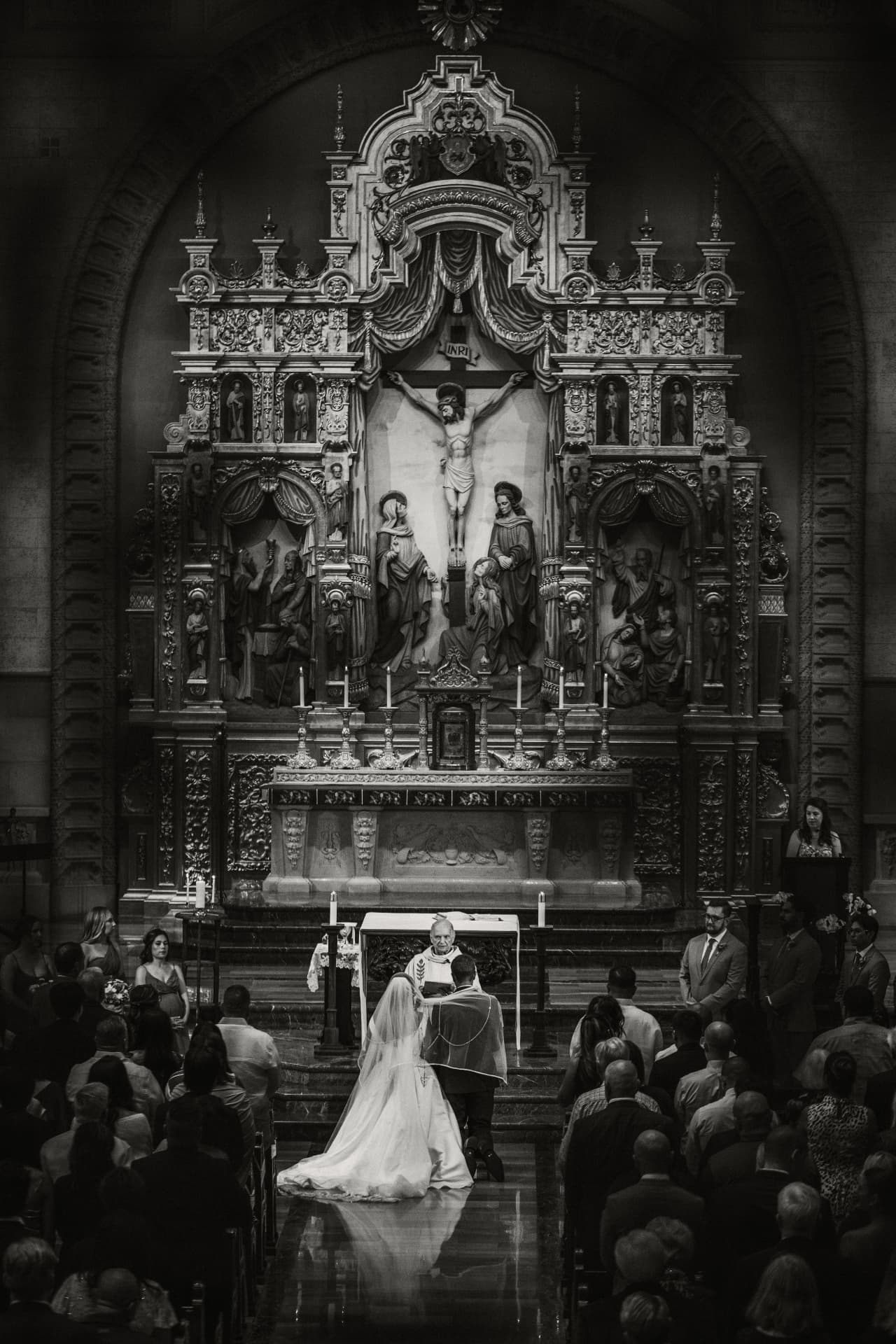 Black and white photo of a couple kneeling before an ornate cathedral altar