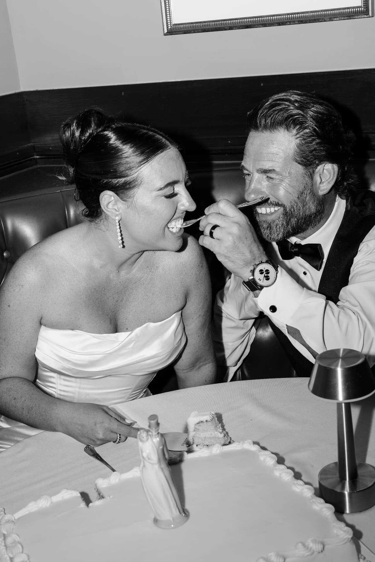 Bride and groom laughing while sharing cake at their reception