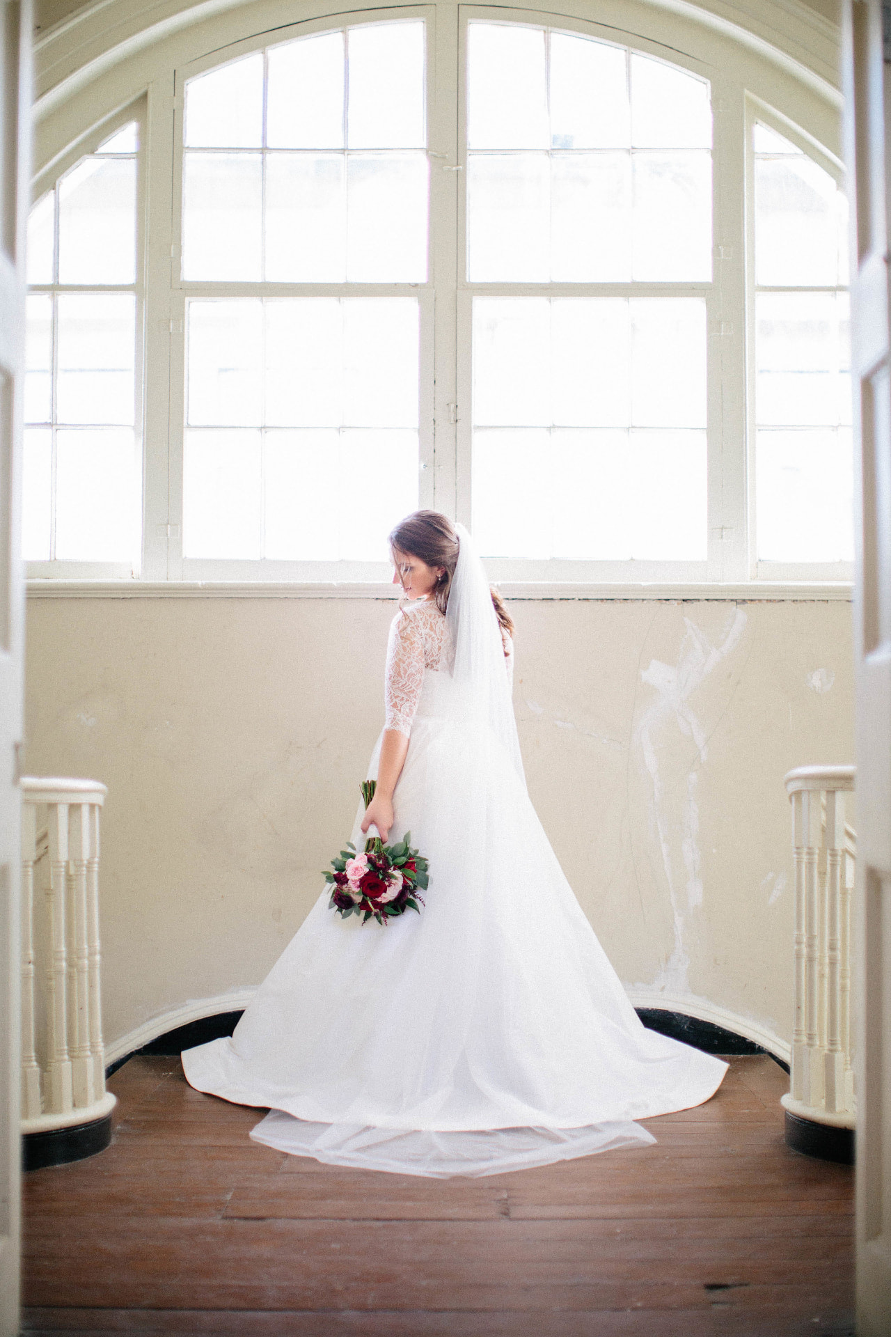 Bride with a long veil and bouquet by an arched window