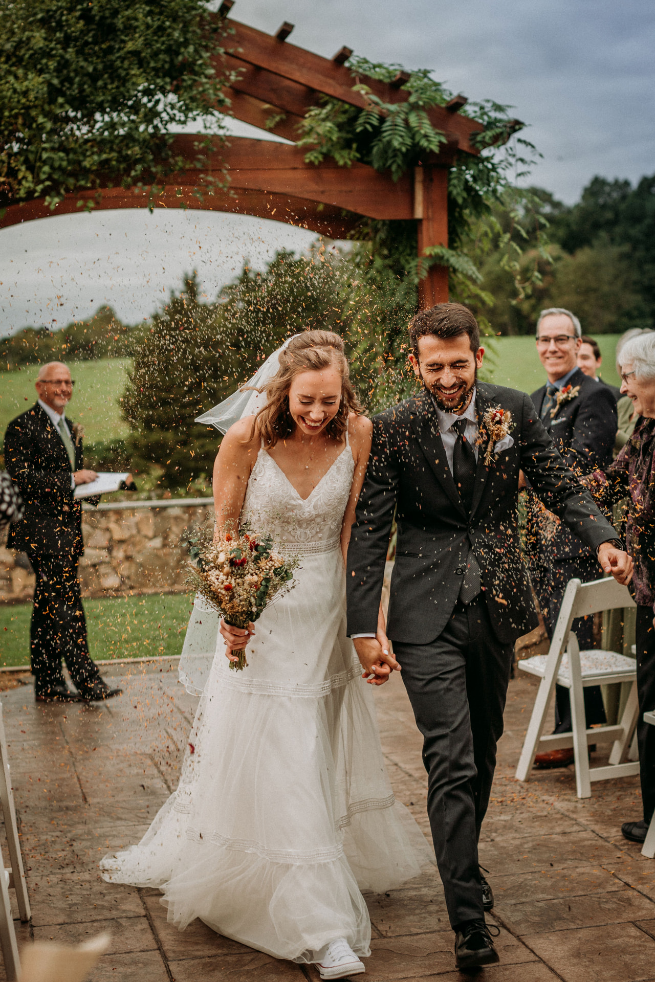 Bride and groom laughing as guests toss petals during the recessional